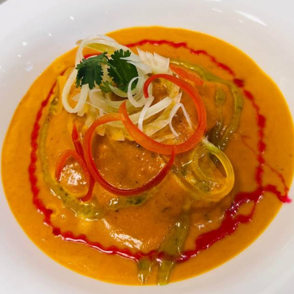 A bowl of rich orange korma topped with sliced peppers and red and green sauces.
